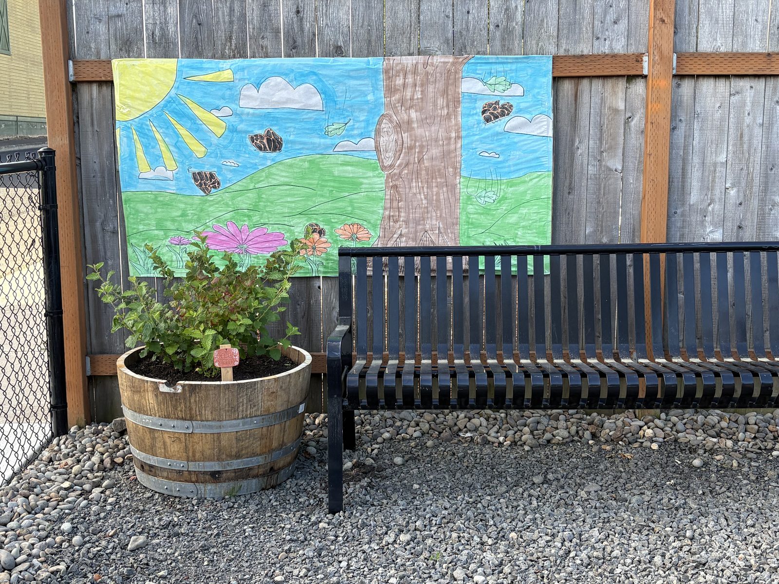 A children's painted mural of a meadow hung on the garden fence behind a bench