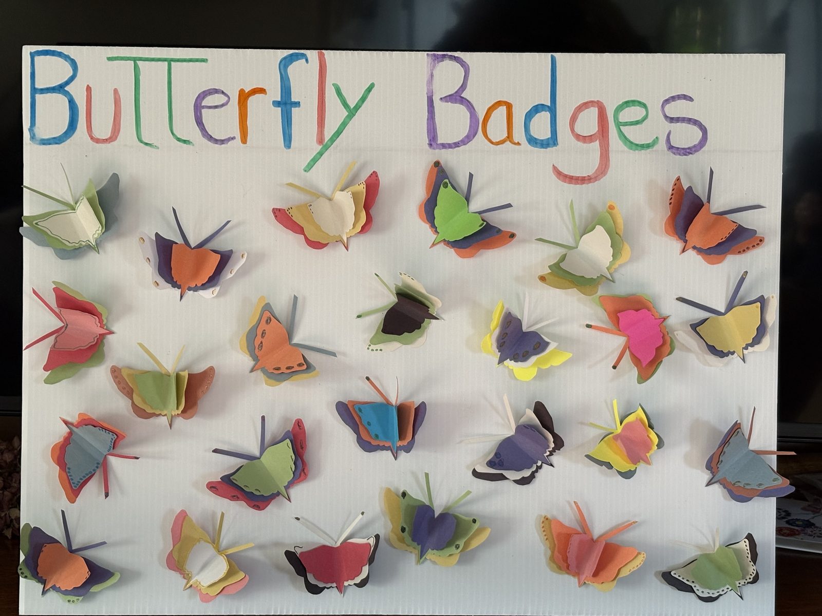 A board covered in folded paper butterfly badges made by children