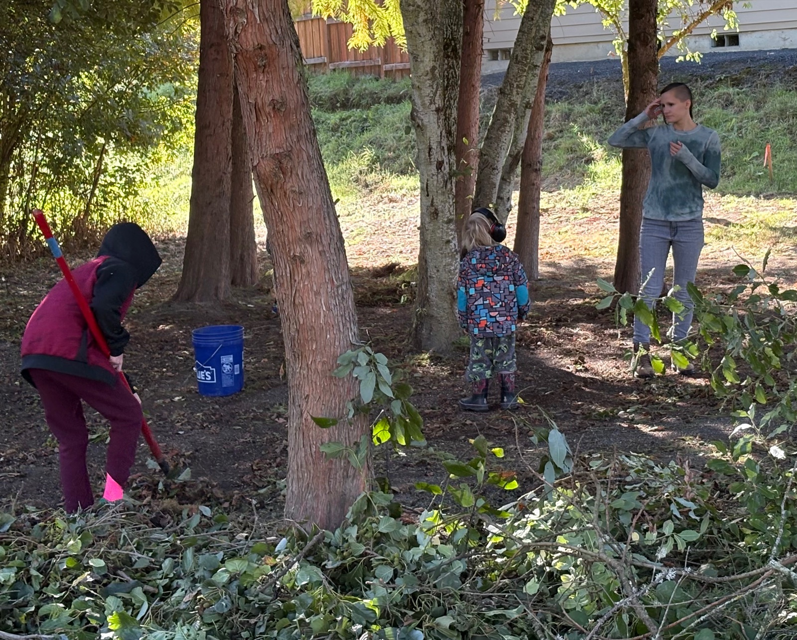 Volunteers young and old raking leaves and clearing cut brush under the trees at Hawn Creek Pocket Park