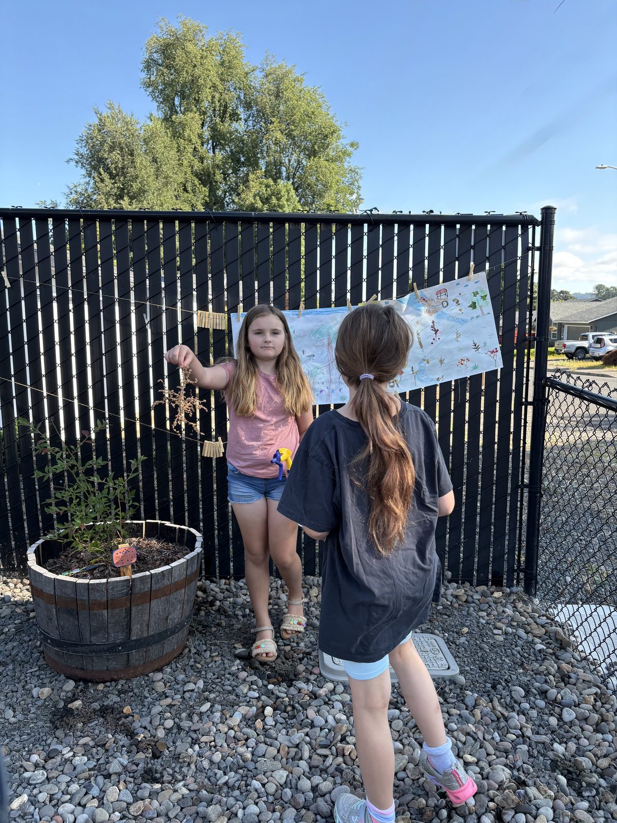 Two children hanging their drawings on the garden fence