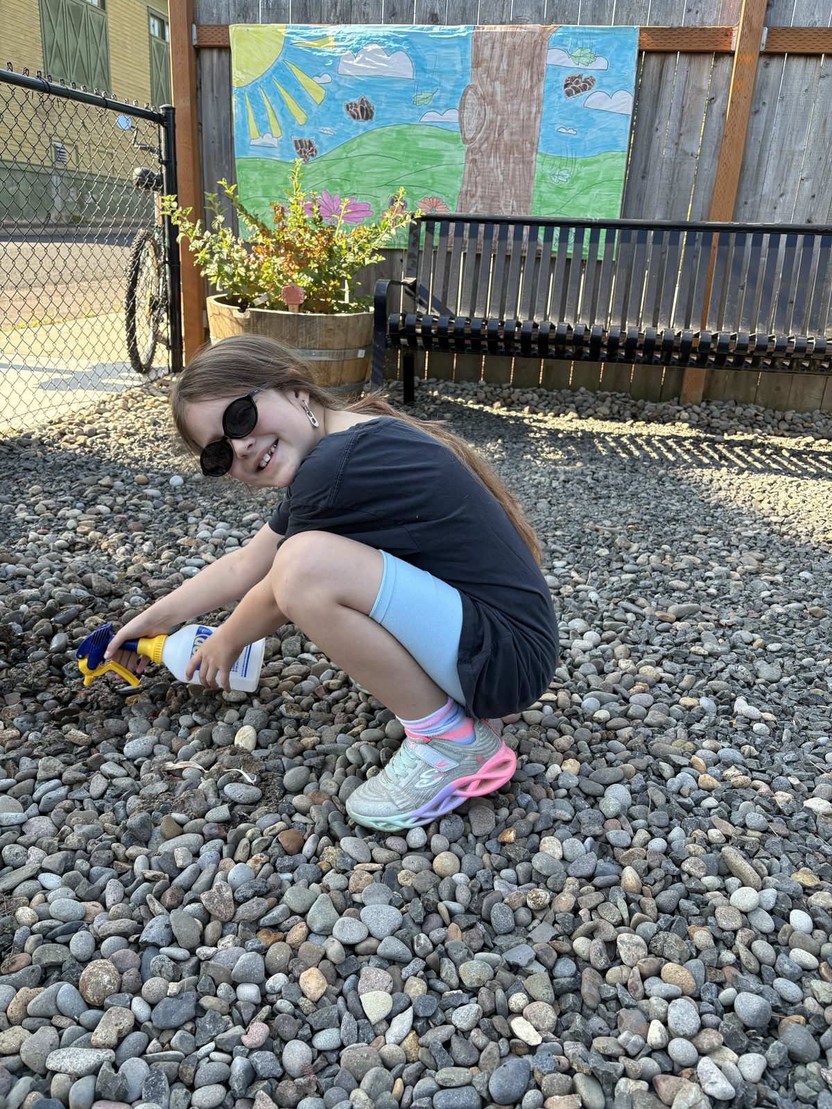 A child crouched on the garden gravel in sunglasses, playing beside the beds