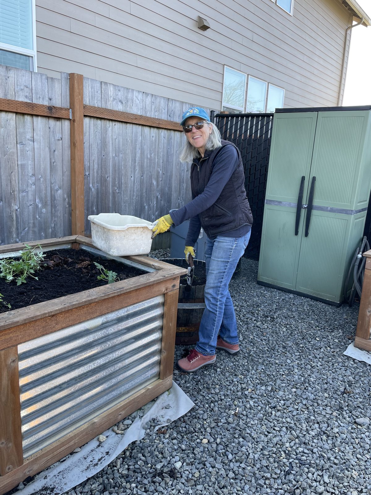 A volunteer in gloves and a cap tipping a tub of soil into a raised garden bed